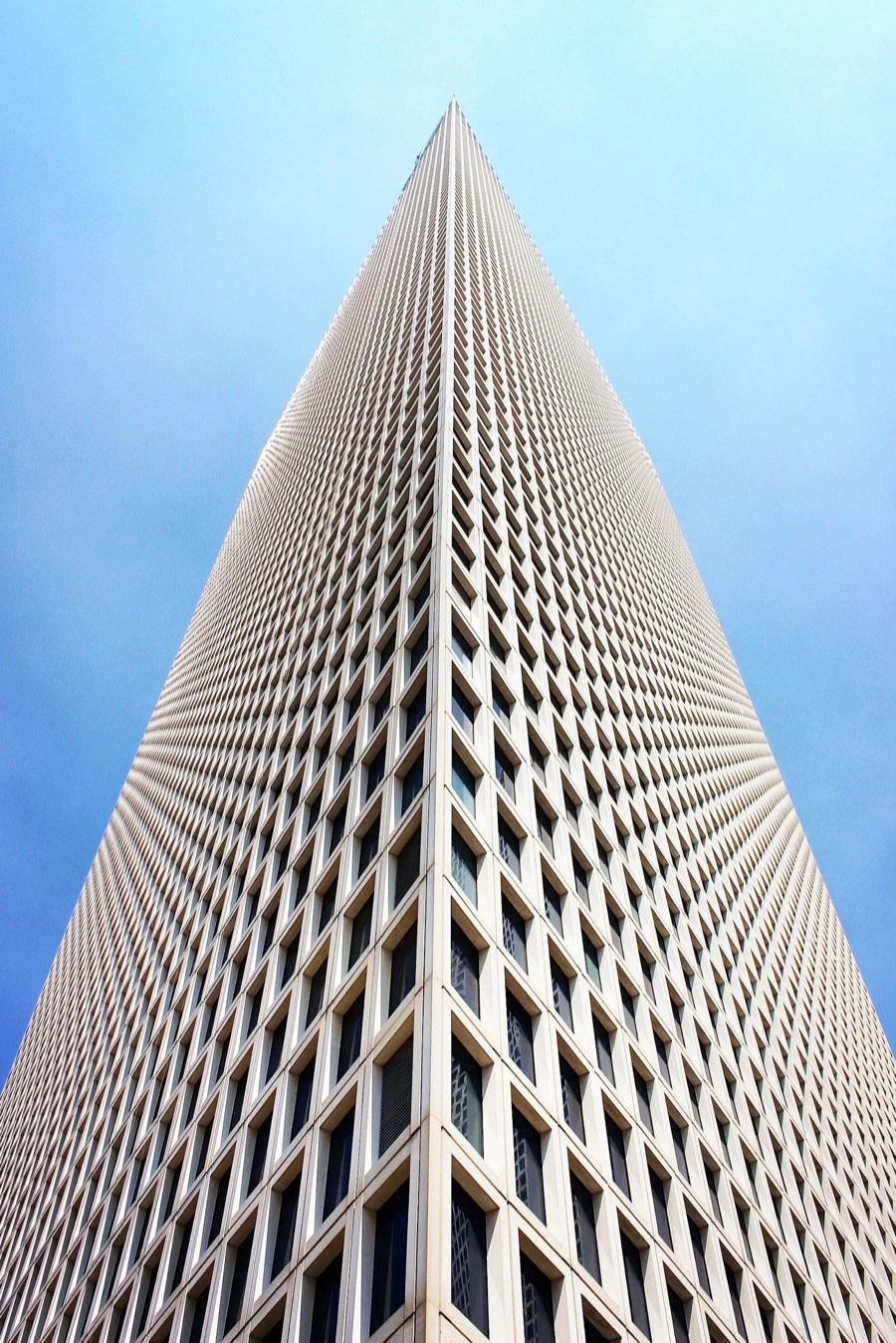 A tall skyscraper viewed from below, with a symmetrical geometric pattern on its facade, set against a clear blue sky.